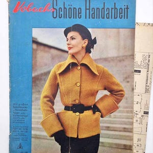 Pode incluir: Uma capa de revista vintage com o título "Vobach Schöne Handarbeit" em vermelho e preto. A capa apresenta uma mulher com um casaco amarelo mostarda com cinto e luvas pretas. A revista é azul e tem texto em alemão.