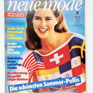Op de afbeelding: Een vintage magazine cover met een lachende vrouw die een kleurrijke gebreide top draagt met vlagachtige ontwerpen. De tijdschrifttitel is "neue mode" met tekst in het Duits. De cover bevat ook tekst over zomermode en handwerken.