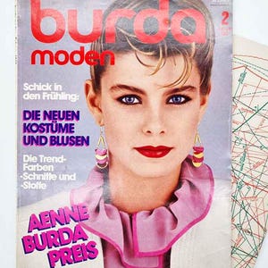May include: A vintage magazine cover with the title "Burda Moden" in red. The cover features a woman with short hair, red lipstick, and blue eyes. German text is visible, along with a pattern sheet on the right side of the image.