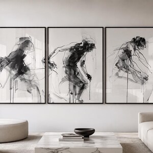 Puede incluir: Tres impresiones artísticas abstractas enmarcadas. Cada impresión presenta un boceto en tinta negra y blanca de una figura humana en movimiento. La obra de arte se exhibe sobre un salón moderno con muebles de tonos neutros.