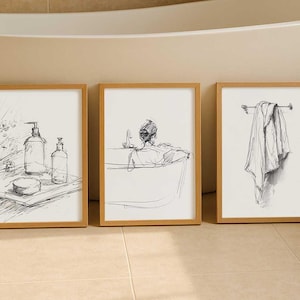 Peut inclure: Trois croquis encadrés en noir et blanc de scènes de salle de bain. L'un montre du savon et des bouteilles, un autre une personne dans une baignoire et le dernier une serviette sur un porte-serviettes. Les cadres sont de couleur marron clair.