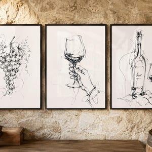 May include: A set of three framed wall art prints featuring black ink line drawings on a white background. The first print shows a cluster of grapes, the second depicts a hand holding a wine glass, and the third shows a wine bottle and glass.