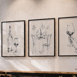 May include: Three framed black and white sketches depicting wine themes. One features a bottle and glass, another a dining table, and the third a hand holding a wine glass. The artwork is displayed on a textured wall.