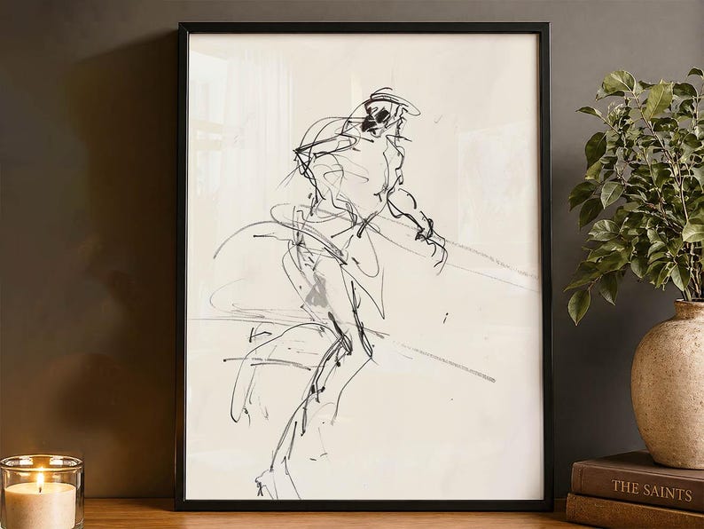 May include: Black framed artwork featuring a sketch of a person in motion. The artwork is a black and white line drawing on a cream-colored background. The frame is black and the artwork is displayed on a wooden surface.