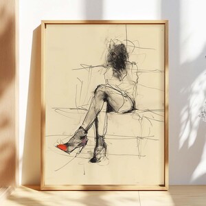 Puede incluir: Un boceto enmarcado de una persona sentada en un sofá, realizado con carboncillo. La obra presenta una figura con rasgos faciales oscurecidos, vestida con un vestido y tacones altos. Un tacón tiene un acento rojo. El boceto está sobre un fondo crema.