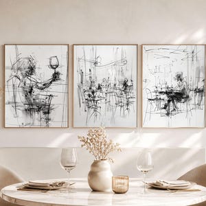 May include: Set of three framed black and white sketches depicting restaurant scenes. The artwork features abstract figures and tables, with a focus on line work and shading. The frames are a light brown color, and the overall theme is a cafe or dining setting.