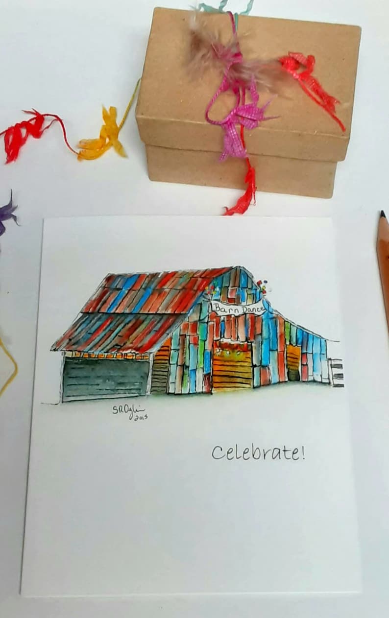 May include: Watercolor painting of a colorful barn with the text "Barn Dance" and "Celebrate!". The barn has a red, blue, and orange roof and multi-colored walls. A small brown gift box with colorful ribbons and feathers sits above the painting.