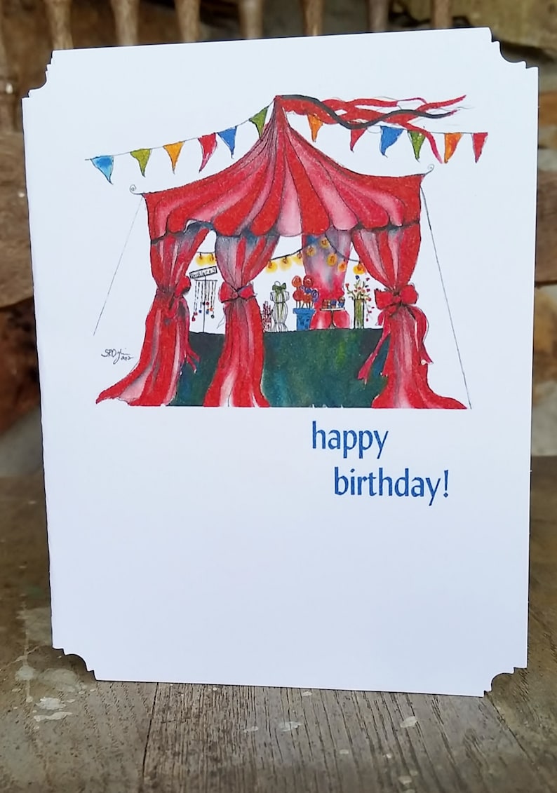 May include: A white birthday card with a watercolor illustration of a circus tent with red curtains and colorful bunting. The text "happy birthday!" is printed in blue.