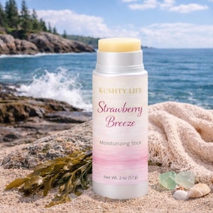 May include: A white and silver moisturizing stick with the text "KUSHTY LIFE Strawberry Breeze Moisturizing Stick". The product is set against a beach backdrop with ocean waves and rocks. The net weight is 2 oz.