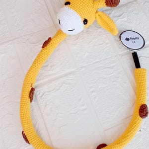 Puede incluir: Un estetoscopio de jirafa de crochet amarillo con manchas marrones. El estetoscopio tiene un tubo negro y una pieza de pecho plateada con el texto "Freely CE" en él.