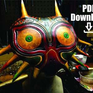 May include: A detailed, hand-painted Majora's Mask replica with sharp, pointed edges and a vibrant color scheme of red, orange, green, and black. The mask is on a display stand and the text "PDF Download" is visible in the upper right corner of the image.