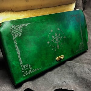 May include: A green leather journal with a decorative silver eye design and a brass clasp.