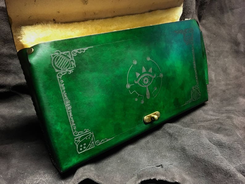 May include: A green leather journal with a decorative silver eye design and a brass clasp.