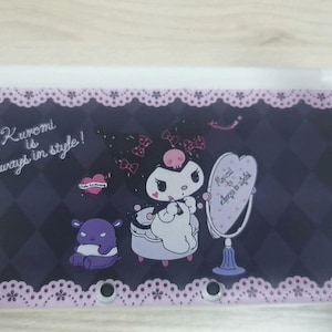 May include: A black and purple Nintendo 3DS case with a cartoon character, a heart, and the text "Kuromi is always in style!". The case has a decorative lace border.