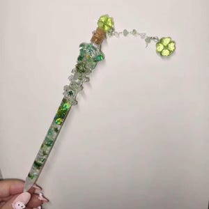 May include: A clear, decorative pen with green shamrock accents. The pen features a cork stopper, green glitter, and a dangling shamrock charm. The pen is designed with a whimsical, handcrafted aesthetic.
