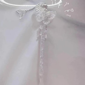Peut inclure: Un stylo décoratif transparent avec un papillon et un charme de queue de sirène. Le stylo présente un motif de papillon en haut, une couronne et un charme de queue de sirène attaché par une chaîne. Le corps du stylo est rempli de paillettes scintillantes.