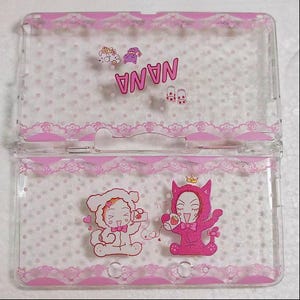 Puede incluir: Funda transparente para teléfono con borde de encaje rosa y diseño de lunares. La funda presenta la palabra "NANA" en rosa, junto con ilustraciones de personajes en ropa rosa y blanca.