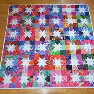May include: A rectangular quilt featuring a repeating star pattern constructed from a grid of multi-colored fabric squares. The design incorporates a wide variety of vibrant colors and diverse patterns, contrasted by solid white eight-pointed stars.