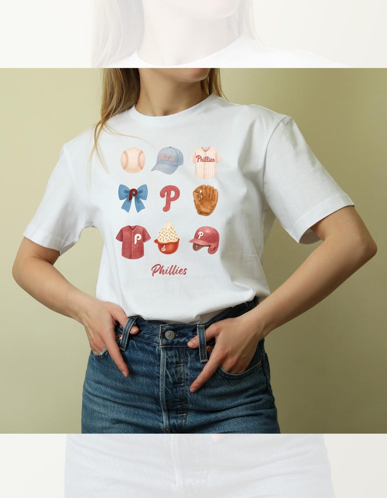 May include: White t-shirt featuring watercolor illustrations of baseball-themed items, including a baseball, cap, jersey, bow, the letter "P", glove, shirt, ice cream, and helmet. The word "Phillies" is printed below the illustrations.
