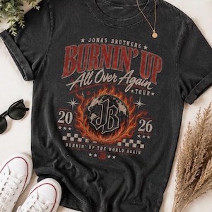 Pode incluir: Uma t-shirt cinzento-carv&atilde;o de manga curta com uma impress&atilde;o gr&aacute;fica que diz Jonas Brothers Burnin' Up All Over Again Tour 2026. O design inclui um globo central rodeado por chamas, as letras JB e um padr&atilde;o de xadrez.