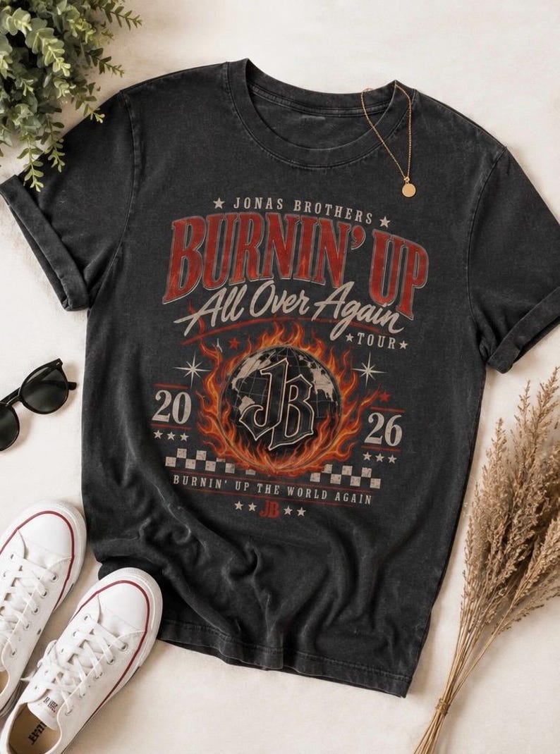 Pode incluir: Uma t-shirt cinzento-carv&atilde;o de manga curta com uma impress&atilde;o gr&aacute;fica que diz Jonas Brothers Burnin' Up All Over Again Tour 2026. O design inclui um globo central rodeado por chamas, as letras JB e um padr&atilde;o de xadrez.