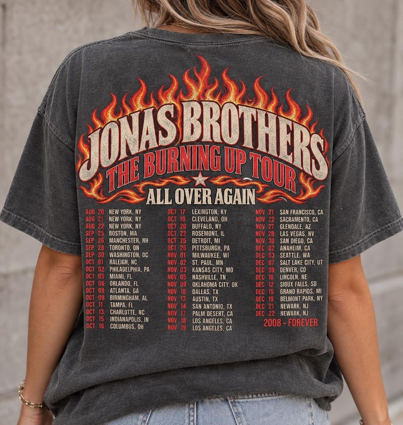 Pode incluir: Uma t-shirt de manga curta cinzento-carv&atilde;o com um gr&aacute;fico nas costas que inclui o texto JONAS BROTHERS THE BURNING UP TOUR ALL OVER AGAIN. O design apresenta chamas cor de laranja e amarelas e uma lista de datas e cidades da digress&atilde;o de 2008.