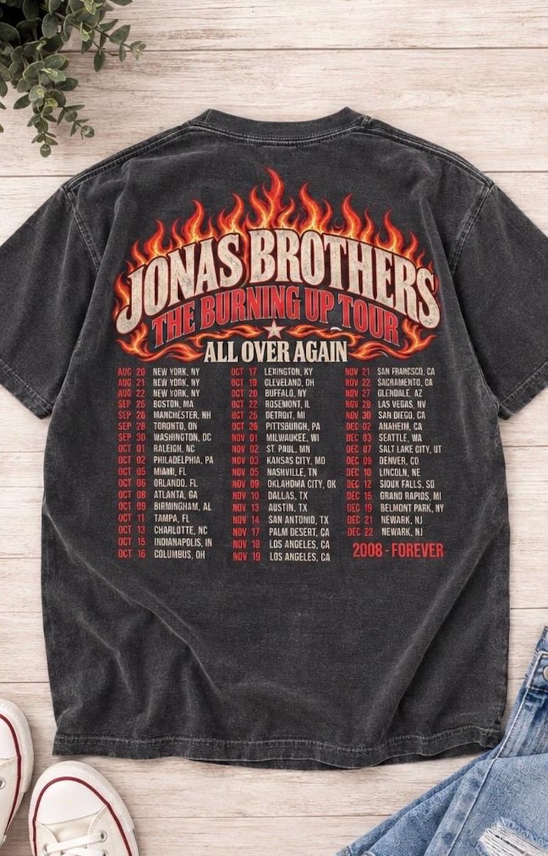 Pode incluir: Uma t-shirt cinzenta escura de manga curta com um gr&aacute;fico nas costas que apresenta chamas cor de laranja e amarelas. O texto diz Jonas Brothers The Burning Up Tour All Over Again, seguido por uma lista de datas e cidades, e 2008-Forever.