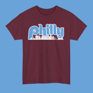 May include: A maroon t-shirt with a blue and white graphic of the Philadelphia skyline and the word "philly" in a retro font.