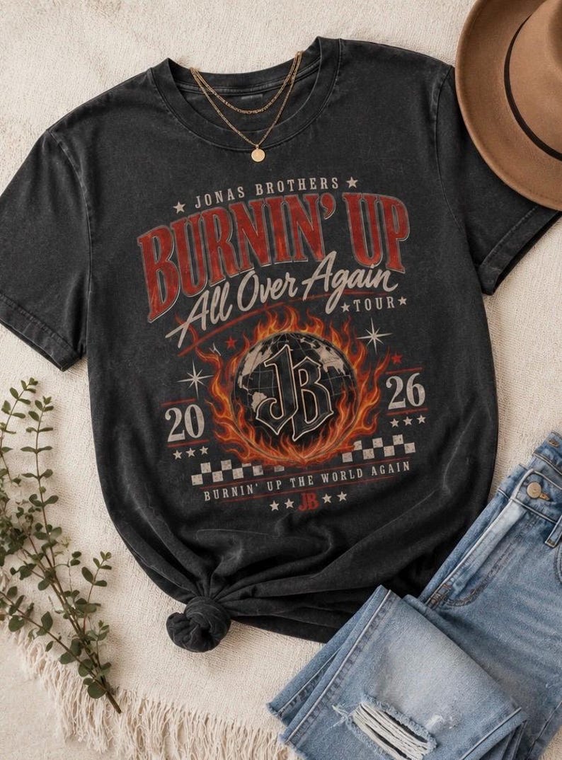 Pode incluir: Uma t-shirt cinzento-carv&atilde;o de manga curta com uma impress&atilde;o gr&aacute;fica com o texto Jonas Brothers Burnin' Up All Over Again Tour 2026. O design inclui um globo rodeado por chamas, um padr&atilde;o axadrezado e as iniciais JB no centro.