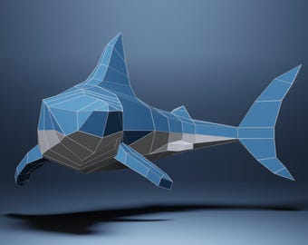 May include: A geometric, low-poly shark sculpture in shades of blue and gray. The shark has a triangular dorsal fin, pectoral fins, and a tail fin. The artwork is set against a gradient blue background, with a shadow.