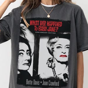Puede incluir: Camiseta gris oscuro con una imagen en blanco y negro de la película "¿Qué fue de Baby Jane?" con Bette Davis y Joan Crawford. El texto "What Ever Happened to Baby Jane? Anniversary Edition" está impreso en rojo.