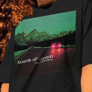 Może przedstawiać: Czarny T-shirt z grafiką okładki albumu "Boards of Canada - Music Has the Right to Children". Okładka albumu przedstawia nocny widok drogi przez las z czerwonymi światłami tylnymi w oddali.