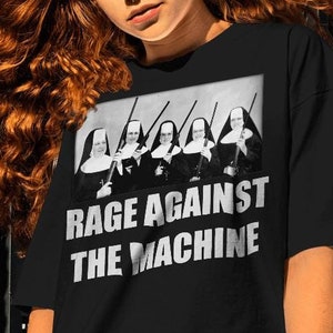 May include: Black t-shirt with a white graphic of five nuns holding rifles. The text "Rage Against The Machine" is printed below the graphic.
