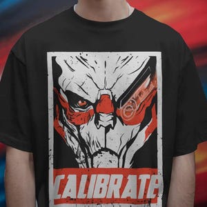 以下が含まれることがあります： 赤と白のロボットの顔のグラフィックと、赤い文字で「CALIBRATE」と書かれた黒いTシャツ。画像に写っている人物は、未来的なシルバーのサングラスをかけています。