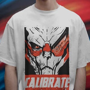 Może przedstawiać: Biały t-shirt z krótkim rękawem z nadrukiem graficznym przedstawiającym stylizowaną, kanciastą twarz stworzenia w kolorach czarnym, białym i czerwonym. Projekt zawiera słowo CALIBRATE wielkimi czerwonymi literami u dołu prostokątnej ramki.