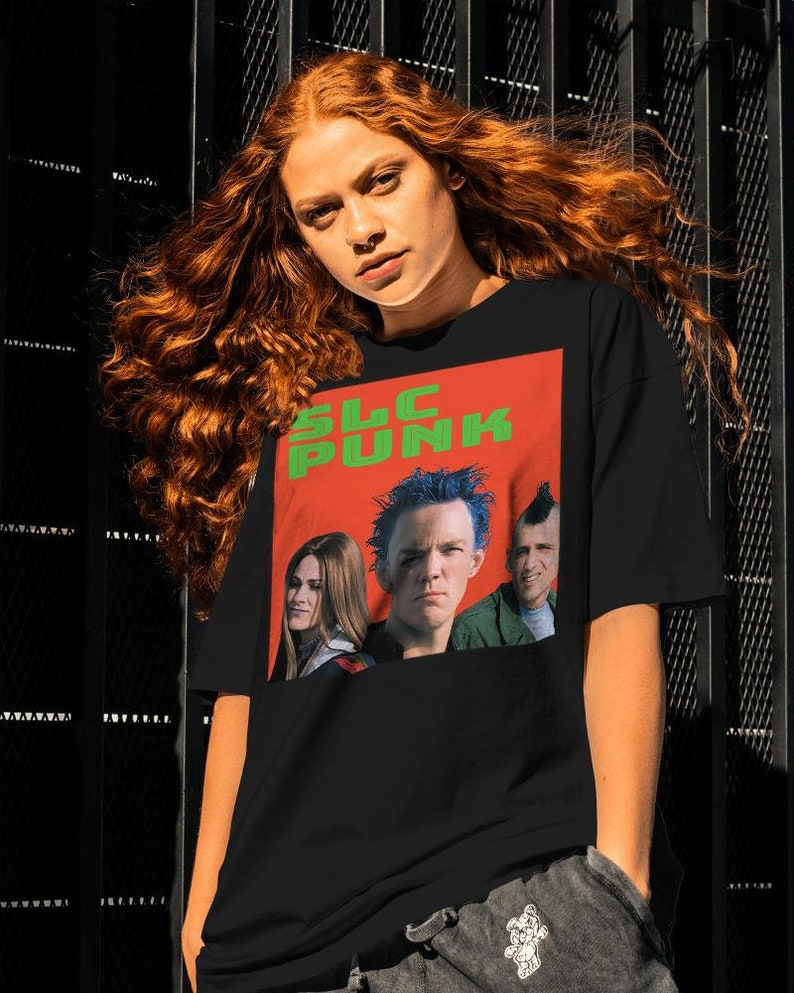 Op de afbeelding: Zwart T-shirt met een rode en groene afbeelding van drie personen met de tekst "SLC PUNK" erop.