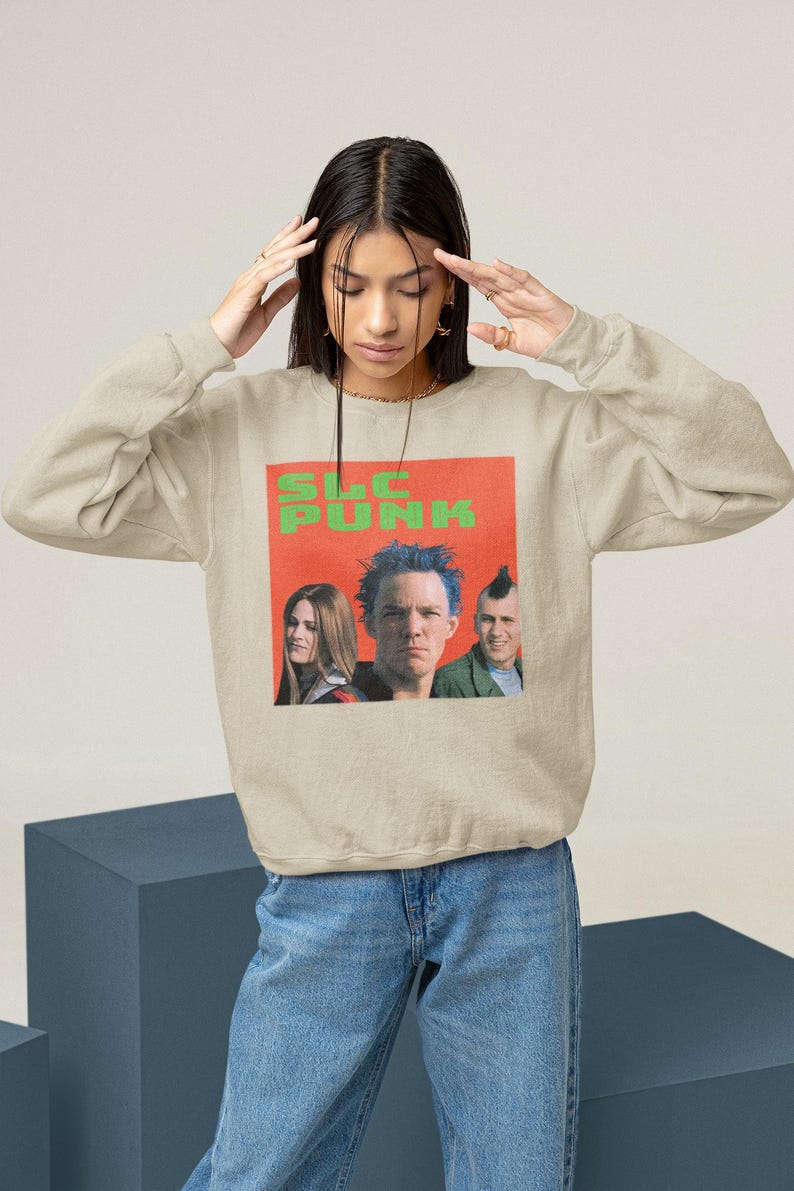 Op de afbeelding: Een beige sweatshirt met een grafische print van een band genaamd "SLC PUNK". De bandleden dragen kleurrijke kleding en hebben punk-kapsels.