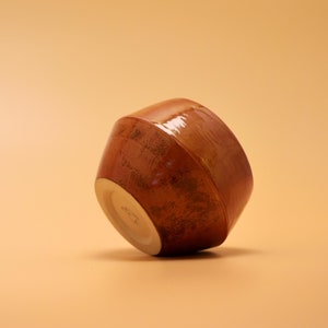 Könnte beinhalten: Eine braune Keramikschüssel mit glasierter Oberfläche. Die Schüssel ist leicht geneigt und der Boden ist sichtbar.