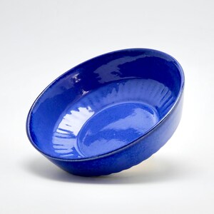 Peut inclure: Un bol en céramique bleu profond et brillant de forme ovale. Le bol a une surface lisse et réfléchissante et un intérieur légèrement texturé. Le bol est incliné, mettant en valeur sa profondeur et son design.
