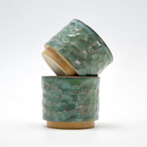 Peut inclure: Deux tasses en céramique faites à la main avec un motif texturé et facetté. Les tasses sont émaillées dans des tons de vert et de turquoise, avec une base marron clair. Une tasse est empilée sur l'autre.