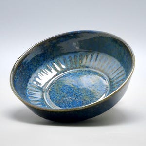 Peut inclure: Un bol en céramique avec un glaçage bleu foncé et un intérieur bleu plus clair. Le bol a une forme légèrement inclinée et une surface texturée, avec un bord foncé. Le bol est adapté pour servir des aliments.