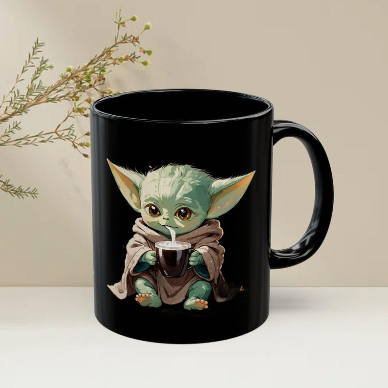 Puede incluir: Taza de cer&aacute;mica negra con una ilustraci&oacute;n de dibujos animados de un personaje alien&iacute;gena verde bebiendo de una taza marr&oacute;n oscuro. El alien&iacute;gena lleva una t&uacute;nica marr&oacute;n y tiene orejas grandes. La taza tiene un asa negra.
