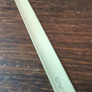 May include: A thin, light brown, rectangular piece of wood with a slightly curved edge. The wood has a smooth, polished surface and is marked with the number "140".