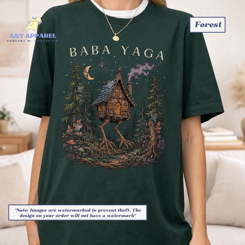 May include: A dark forest green t-shirt featuring a graphic print of a wooden hut on chicken legs in a forest setting. The text BABA YAGA is printed above the hut, which is surrounded by trees, a crescent moon, and smoke in the night sky.