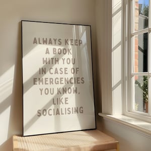 Könnte beinhalten: Ein schwarzer gerahmter Druck mit dem Text "ALWAYS KEEP A BOOK WITH YOU IN CASE OF EMERGENCIES YOU KNOW, LIKE SOCIALISING" in brauner Schrift auf weißem Hintergrund.