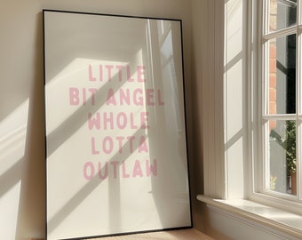 May include: A black framed print with the text "LITTLE BIT ANGEL WHOLE LOTTA OUTLAW" in pink lettering on a white background.