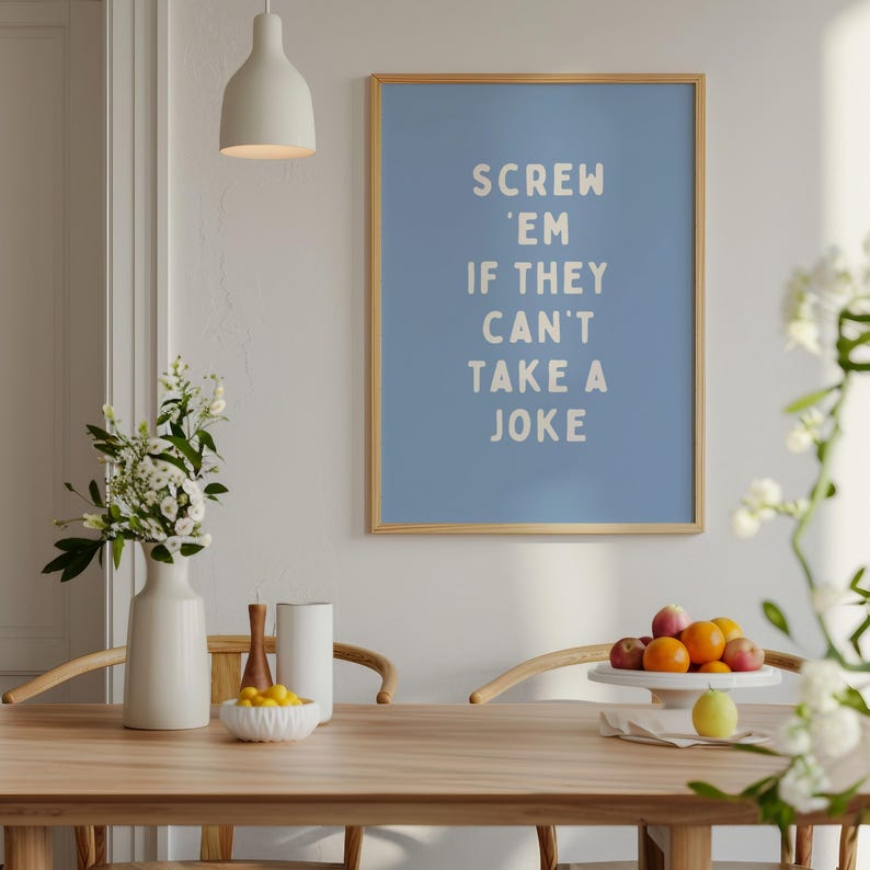 May include: A framed poster with the text "Screw 'em if they can't take a joke" in white letters on a light blue background. The poster is in a room with a wooden table, white vase, and a bowl of lemons.