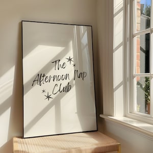 May include: A framed print with a white background and black text that reads "The Afternoon Nap Club" with two stars on either side of the text.
