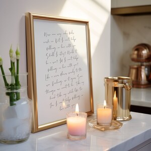 May include: A gold framed print with a handwritten poem about falling in love. The poem is set on a white countertop with two lit candles and a gold metal ice bucket.