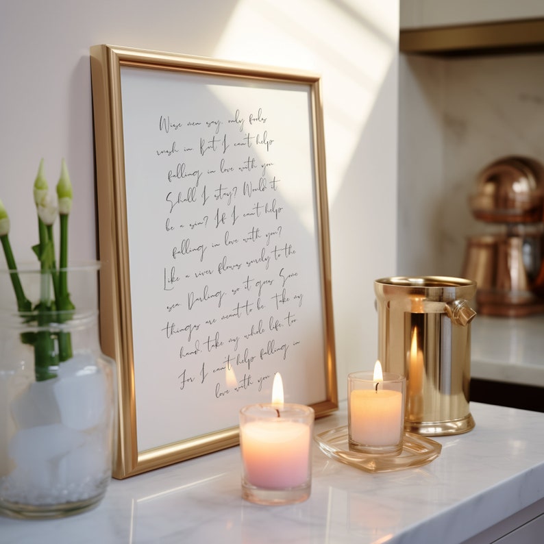 May include: A gold framed print with a handwritten poem about falling in love. The poem is set on a white countertop with two lit candles and a gold metal ice bucket.
